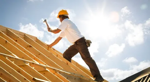 Tradie standing on top of a roof under construction, hammer raised 